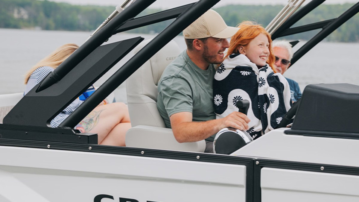 Family boating trip: two adults and a child sitting together on a white boat, enjoying a lake view.