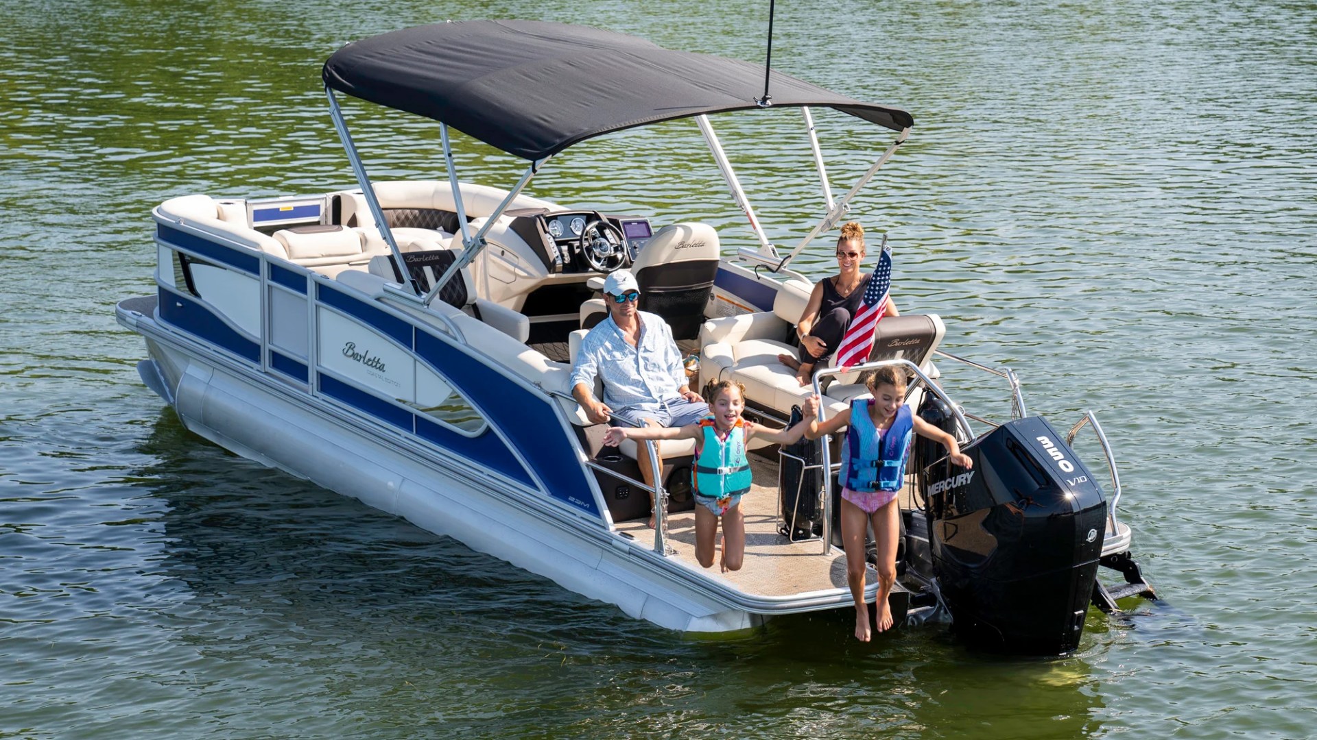 Family on motorboat with two children in life jackets at rear; American flag visible.