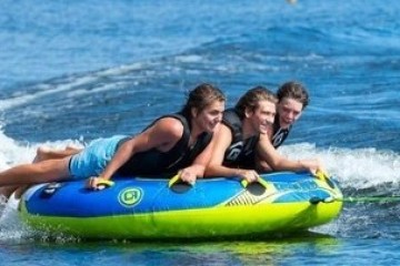 Three people tubing on water, smiling and holding onto a large inflatable.