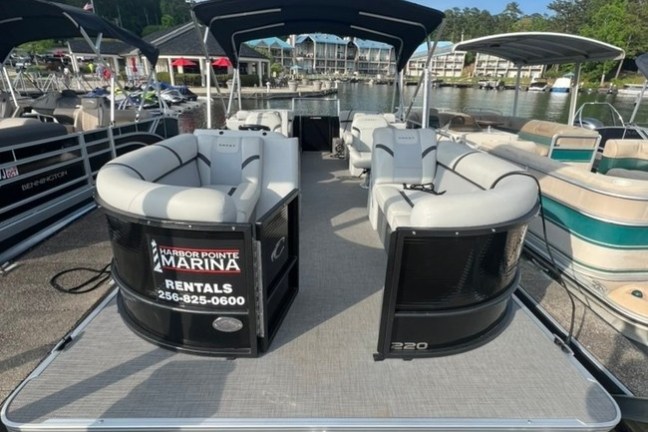 Pontoon boat docked at marina with shaded seating and rental sign.
