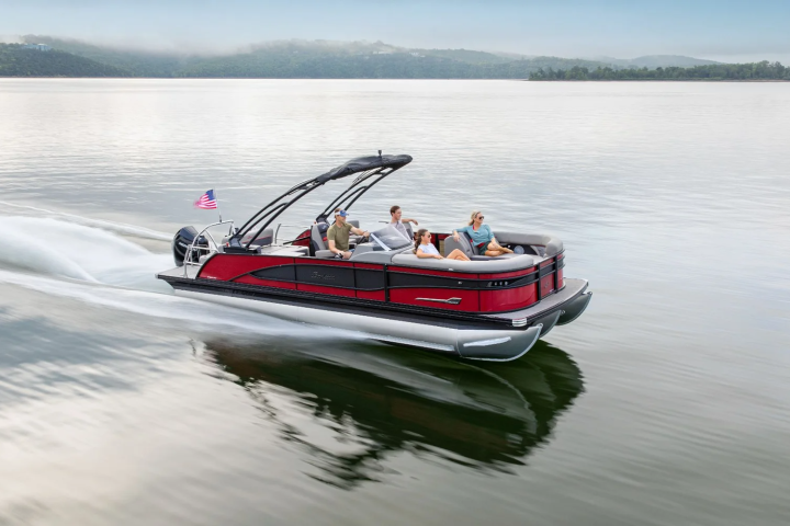 People riding a red pontoon boat on a calm lake with an American flag waving.