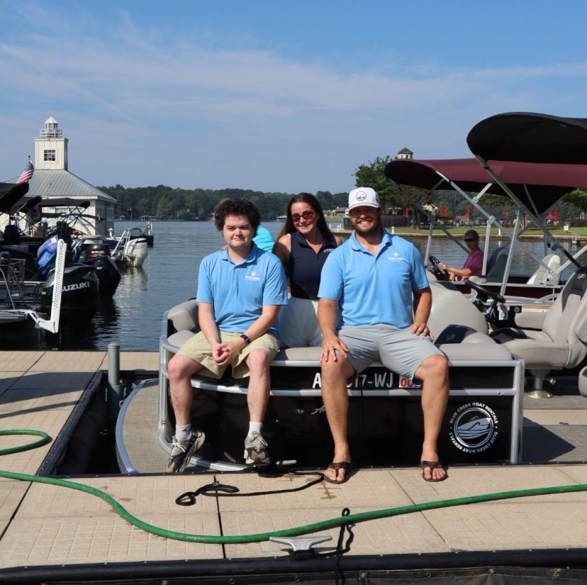 Three people in blue shirts sit on a docked boat on a sunny day.