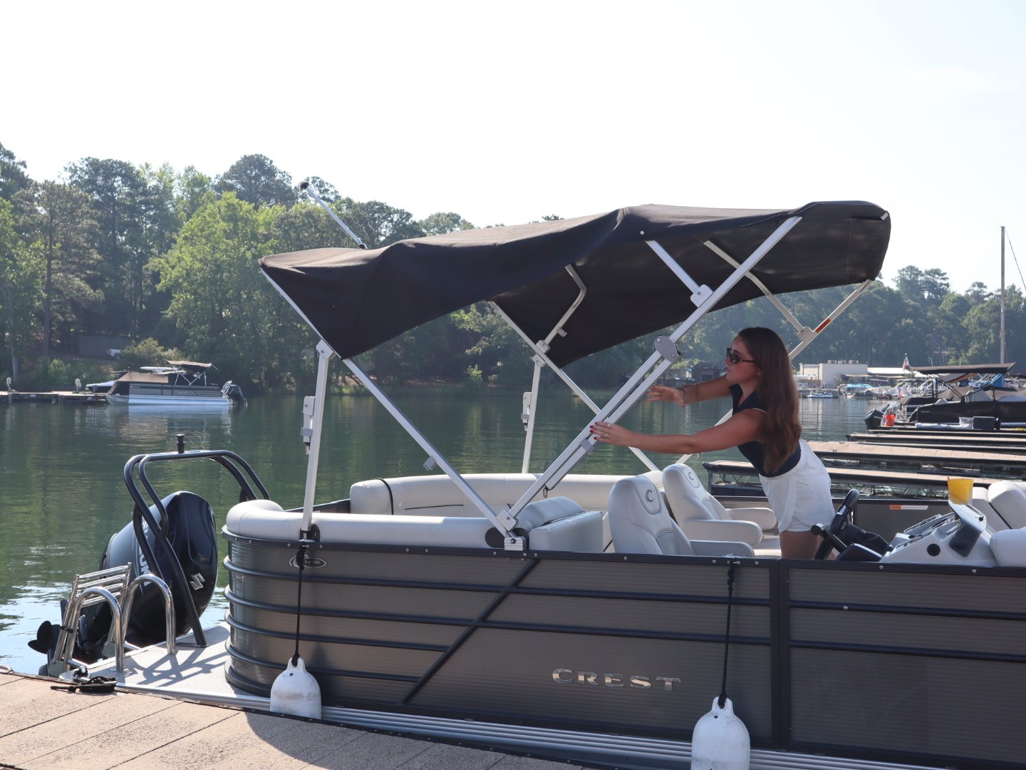 Woman adjusting canopy on a pontoon boat docked by a lake.