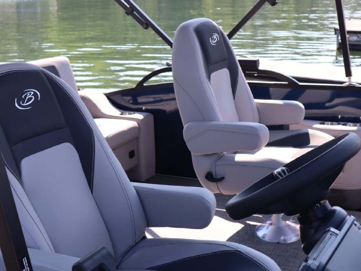 Interior of a boat with two seats and a steering wheel near a calm lake.